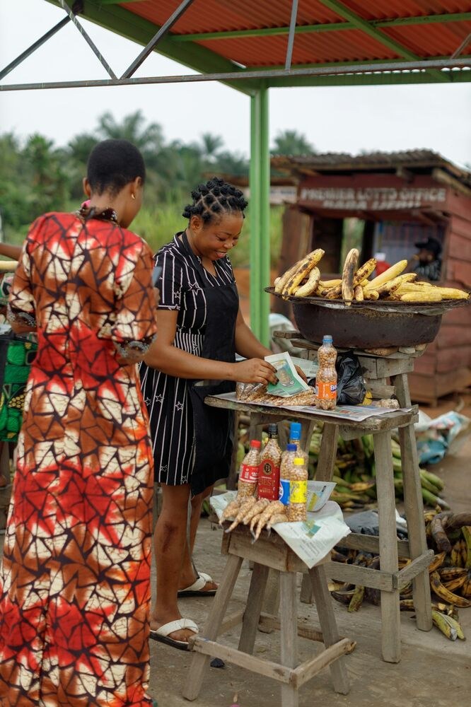 A food stall vendor serves a customer at a roadside plantain stand